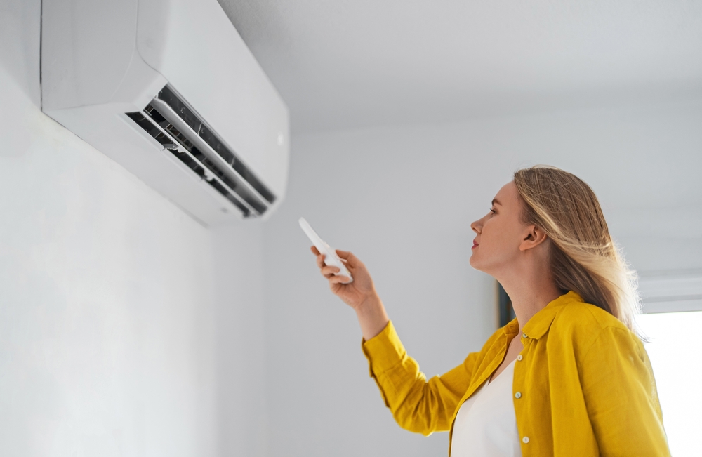 Woman,Holding,Remote,Control,Aimed,At,The,Air,Conditioner.